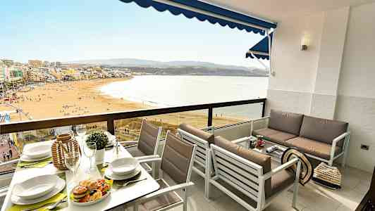 Et møblert balkongområde med utsikt over en strand og havet. (AI-generert tekst)