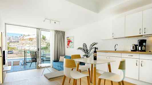 Lyst møblert hotellrom med kjøkkenkrok og balkong med utsikt. (AI-generert tekst)