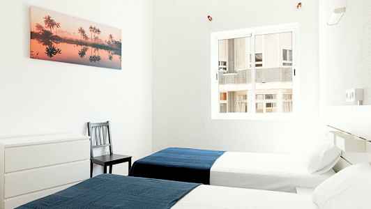 To enkeltsenger i et lyst rom med et blått teppe på hver seng. (AI-generert tekst)