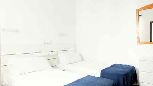 To enkeltsenger med hvite laken og blå tepper i et hotellrom. (AI-generert tekst)