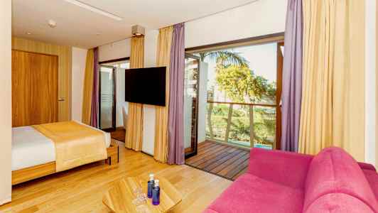 Hotellrom med seng, rosa sofa, TV og balkong. (AI-generert tekst)