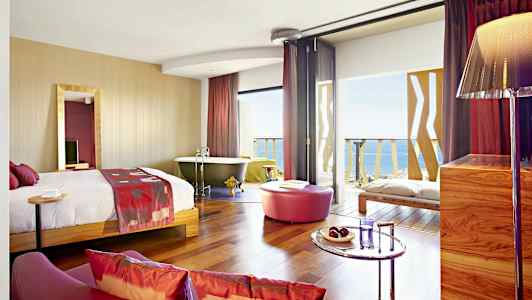 Et hotellrom med en seng, badekar, sittegruppe og utsikt over havet. (AI-generert tekst)