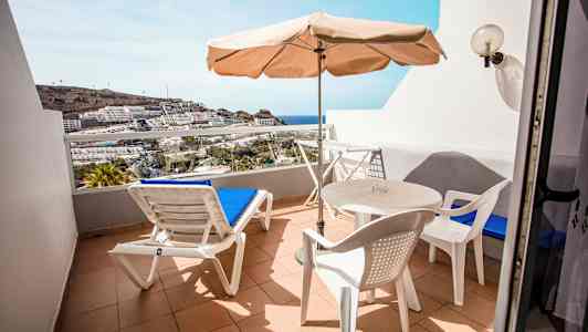 En terrasse med solsenger, bord og stoler samt utsikt over havet og bygninger. (AI-generert tekst)