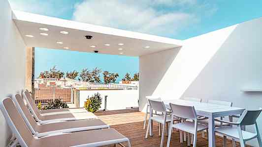 Terrasse med solsenger og et spisebord med stoler under en hvit takoverbygning. (AI-generert tekst)