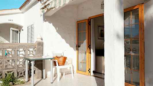 Terrasse med hvit bygning, bord og stol, samt en dør som fører inn i huset. (AI-generert tekst)