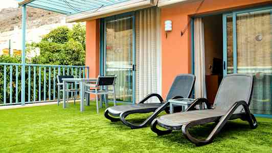 En terrasse med solsenger og et bord med stoler, samt grønn kunstig plen. (AI-generert tekst)