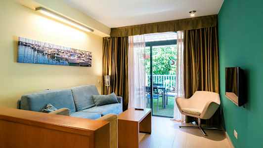 Stue med blå sofa, beige stol og store vinduer som vender ut mot en balkong. (AI-generert tekst)