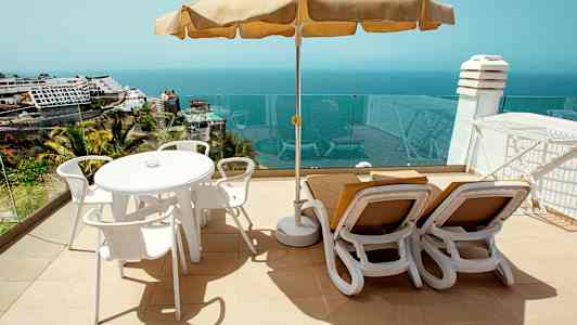 Solterrasse med bord, stoler og solsenger samt havutsikt. (AI-generert tekst)