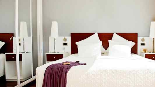 Et hotellrom med en dobbeltseng med hvitt sengetøy og puter samt et teppe med et drapert teppe. (AI-generert tekst)