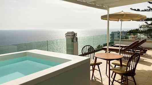 Terrasse med et lite basseng, bord og stoler samt solsenger med utsikt over havet. (AI-generert tekst)