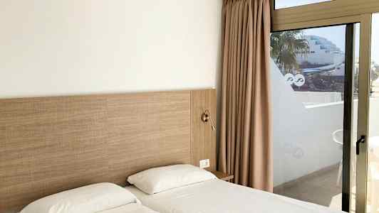 To enkeltsenger med hvitt sengetøy ved siden av en glassdør med utsikt. (AI-generert tekst)