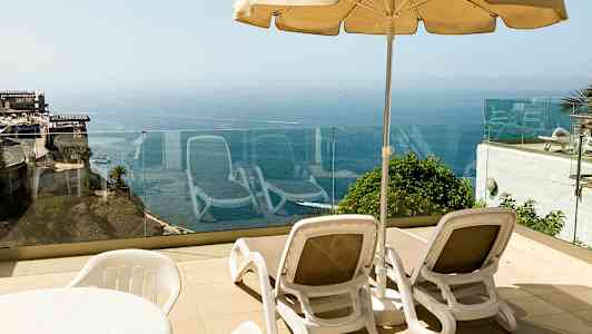 To solsenger med parasoll på en terrasse med havutsikt. (AI-generert tekst)