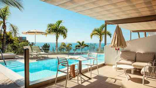 En terrasse med et basseng og utsikt over havet, omgitt av palmer. (AI-generert tekst)