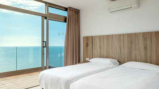 Et hotellrom med to enkeltsenger og utsikt over havet gjennom store vinduer. (AI-generert tekst)