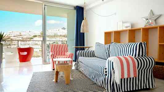 En stue med en sofagruppe foran en glassdør som leder til en balkong. (AI-generert tekst)