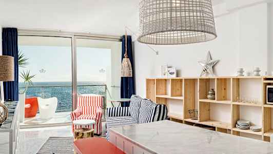 Utsikt over en moderne stue med maritim innredning og havet synlig gjennom glassdører. (AI-generert tekst)