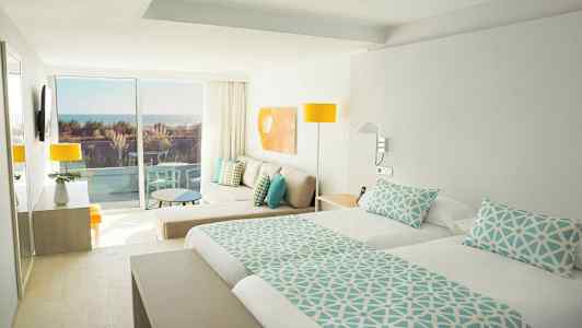 Lyst hotellrom med dobbeltseng, sittegruppe og balkong med havutsikt. (AI-generert tekst)