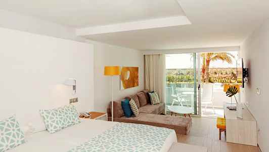 Et moderne hotellrom med seng, sofa, dekorativt trebord og balkong med utsikt. (AI-generert tekst)