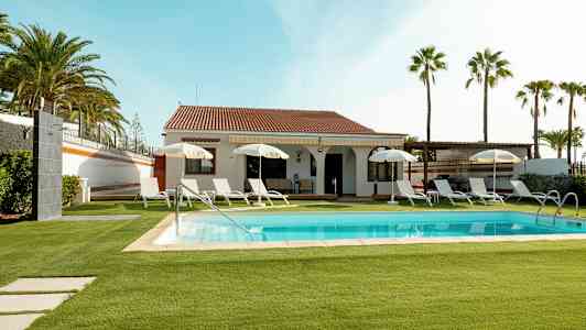 Villa med basseng og solsenger, omgitt av plen og palmer. (AI-generert tekst)