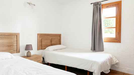 Et rom med to enkeltsenger, tredetaljer og et vindu med grå gardiner. (AI-generert tekst)