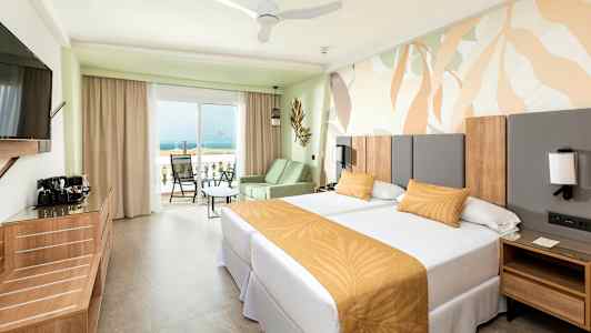 Hotellrom med to enkeltsenger og en balkong med utsikt over havet. (AI-generert tekst)