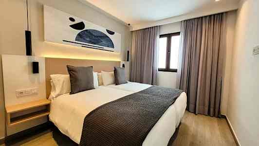 Et moderne hotellrom med to enkeltsenger, kunst på veggen og et vindu med gardiner. (AI-generert tekst)