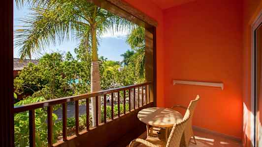 Balkong med to flettede stoler og bord, omgitt av planter og palmer. (AI-generert tekst)