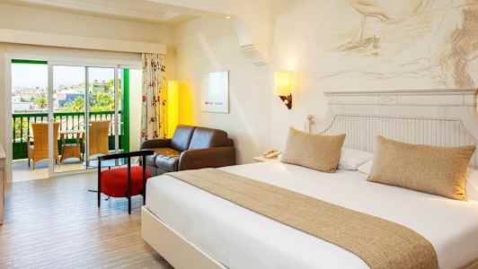 Et hotellrom med en dobbeltseng, en sittegruppe og en balkong. (AI-generert tekst)