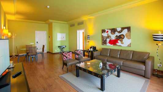 Stue med grønn vegg, brun sofa, kunst på veggen og et spisebord med stoler. (AI-generert tekst)