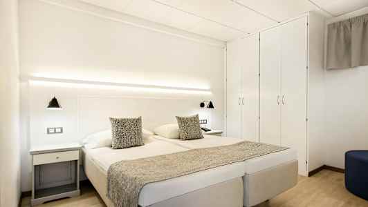 Dobbeltrom med hvite vegger, dobbeltseng, sengelamper og garderobe. (AI-generert tekst)