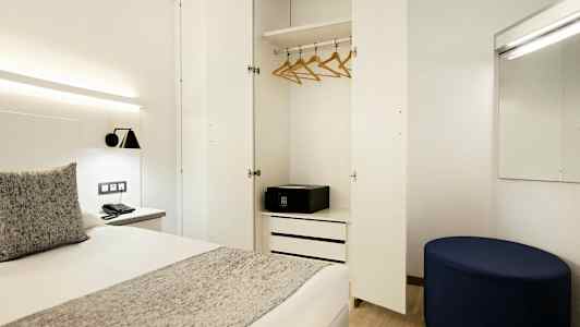 Et hotellrom med åpen garderobe, seng og speil. (AI-generert tekst)