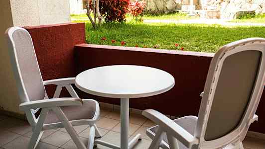 To sitteplasser med bord på en balkong med utsikt mot plen og steinmur. (AI-generert tekst)