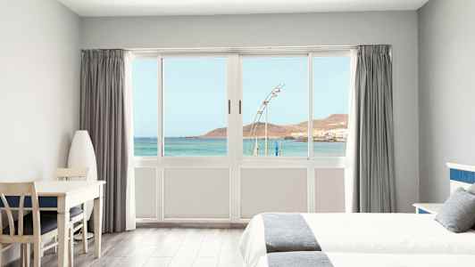 Lyst hotellrom med utsikt over havet gjennom en stor vindusfront. (AI-generert tekst)