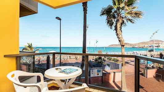 Utsikt fra en balkong med bord og stoler mot havet og stranden. (AI-generert tekst)