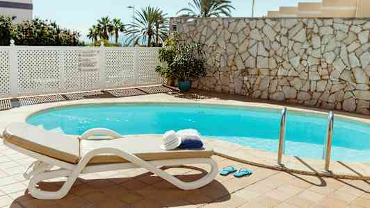 Utendørsbasseng med solseng og en stabel med håndklær og hatt. (AI-generert tekst)