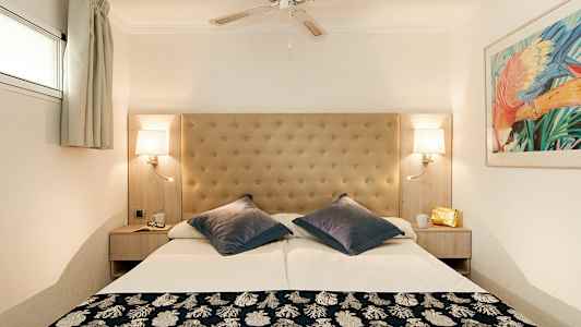 Et hotellrom med en dobbeltseng, polstret sengegavl, takvifte og vegglamper. (AI-generert tekst)