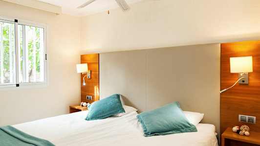 Et lyst soverom med en dobbeltseng, blå puter og vindu. (AI-generert tekst)