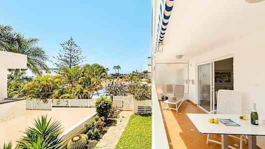 En uteplass med stol og bord, utsikt til en hage og palmer. (AI-generert tekst)