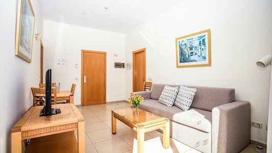 Et hotellrom med en sofa, et spisebord og en TV. (AI-generert tekst)