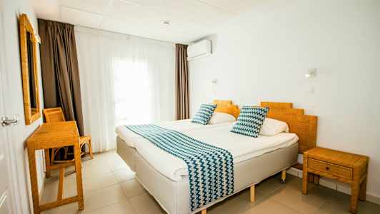 Et hotellrom med to enkeltsenger, bambusmøbler og hvite vegger. (AI-generert tekst)