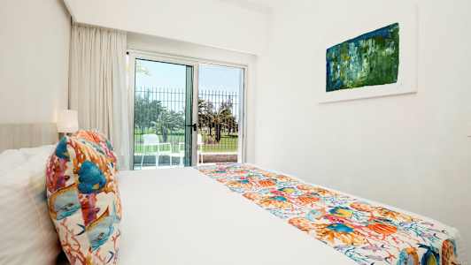 Et lyst hotellrom med en seng, fargerike dekorasjoner og en utgang til en terrasse. (AI-generert tekst)