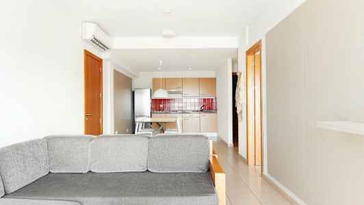 Bilde av en lys stue med en grå sofa i forgrunnen og et kjøkken i bakgrunnen. (AI-generert tekst)