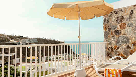 Utsikt fra en terrasse med en solseng, parasoll og hav i bakgrunnen. (AI-generert tekst)