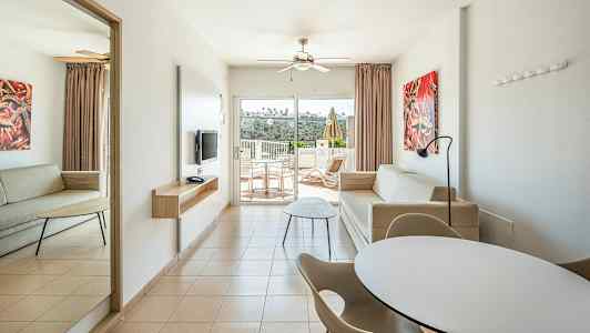 Et moderne hotellrom med to sofaer, spisebord og stoler samt en balkong med utsikt. (AI-generert tekst)