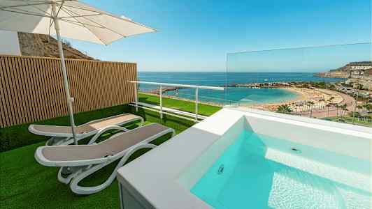 Terrasse med solsenger, parasoll og lite basseng med utsikt over strand og hav. (AI-generert tekst)