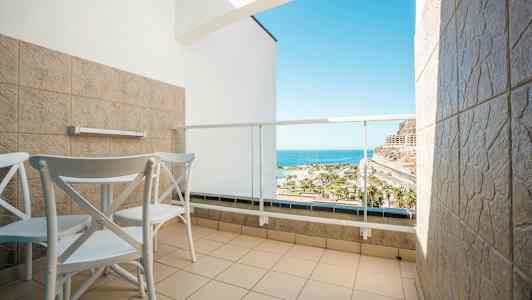 Hotellbalkong med to stoler og bord, med utsikt over havet. (AI-generert tekst)