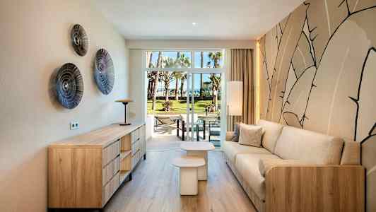 En moderne innredet stue med tredetaljer og en beige sofa, utsikt mot en grønn hage gjennom glassdører. (AI-generert tekst)