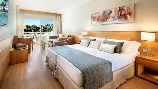 Et hotellrom med en dobbeltseng, sittegruppe og balkong med utsikt. (AI-generert tekst)