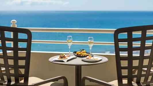 To tallerkener med mat og to glass med drikke på et bord med havutsikt. (AI-generert tekst)