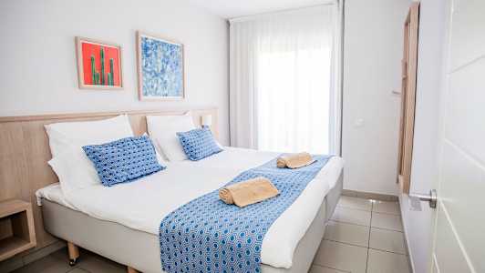 Bilde av et hotellrom med en dobbeltseng, blå detaljer og kunstverk på veggen. (AI-generert tekst)